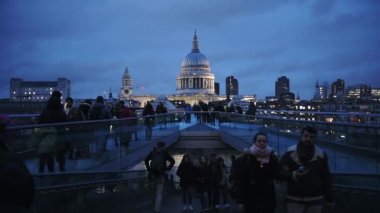 People Walking At The Millenium Bridge In London, UK At Dusk With The Famous Saint Paul's Cathedral In The Background - Wide Shot