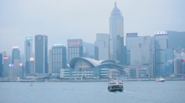 Ferry Boat Cruising On The Victoria Harbour With Hong Kong Skyline On The Background. - wide shot