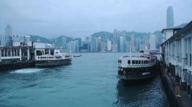 Two Star Ferry Boat Moored On The Pier In Victoria Harbour With Skyline Of Hong Kong On The Background.- wide shot
