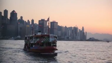 A Ferry Boat Smoothly Sailing Across The Calm Sea In Hong Kong On A Sunset With High Rise Buildings In The Background - Medium Shot
