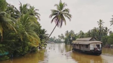 Landscape view of a houseboat floating on a river flowing through palm trees, Kerala Backwaters, India