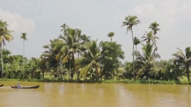 Local men on traditional boats on a river flowing near palm trees, Kerala Backwaters, India
