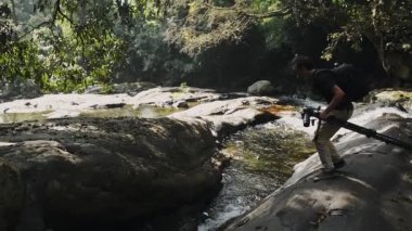Photographer jumping from a rock to another in the middle of a river, in Munnar, India