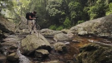 Photographer taking pictures on a rock in the middle of a river, in Munnar, India