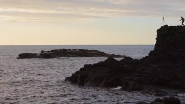 Silhouette Of A Landscape Photographer Shooting The Beautiful Sunset And Coast On The Edge Of The Cliff With The Camera On Tripod In Atrim Coast, Northern Ireland.- wide shot