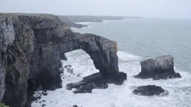 Rough waves crashing on Green Bridge, Pembrokeshire Coast National Park, Wales, on a moody day