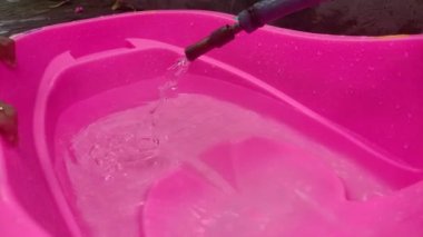 Çocuk suda oynuyor ve pembe plastik bebek küvetinde banyo yapmaya hazır.