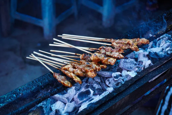 Chicken satay on charcoal fire. Hands cooking satay on the grill. Satay on fire with smoke and an appetizing look.