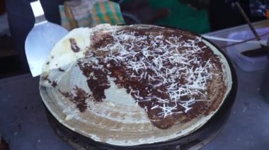 makes a crepe pancake on a baking tray in a creperie, give chocolate with cheese topping