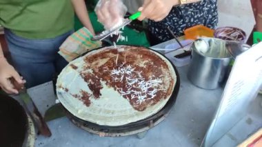 makes a crepe pancake on a baking tray in a creperie, give chocolate with cheese topping