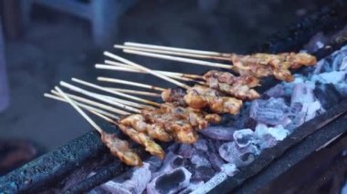 Chicken satay on charcoal fire. Hands cooking satay on the grill. Satay on fire with smoke and an appetizing look.