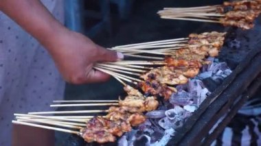 Chicken satay on charcoal fire. Hands cooking satay on the grill. Satay on fire with smoke and an appetizing look.