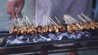 Chicken satay on charcoal fire. Hands cooking satay on the grill. Satay on fire with smoke and an appetizing look.