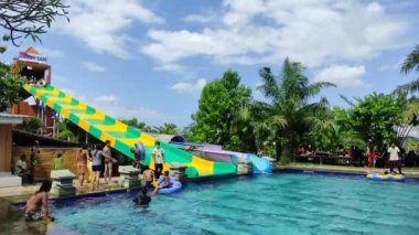 Badung, Bali, Indonesia - July 9, 2022: Visitors play in the outdoor water park featuring a swimming pool and waterslide, attractions for large and small.