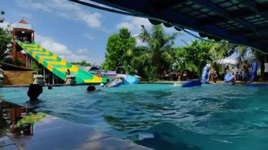 Badung, Bali, Indonesia - July 9, 2022: Visitors play in the outdoor water park featuring a swimming pool and waterslide, attractions for large and small.