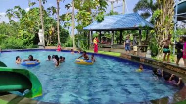 Badung, Bali, Indonesia - July 9, 2022: Visitors play in the outdoor water park featuring a swimming pool and waterslide, attractions for large and small.
