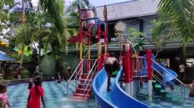 Badung, Bali, Indonesia - July 9, 2022: Visitors play in the outdoor water park featuring a swimming pool and waterslide, attractions for large and small.