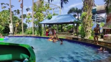 Badung, Bali, Indonesia - July 9, 2022: Visitors play in the outdoor water park featuring a swimming pool and waterslide, attractions for large and small.