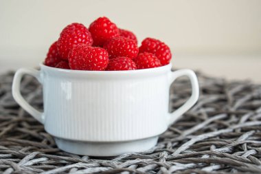 Fresh raspberries in the white bowl on the gray background.