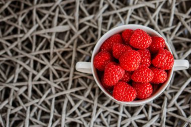 Fresh raspberries in the white bowl on the gray background, top view