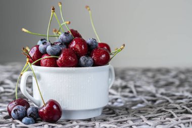 Ripe organic cherries and blueberries on gray background with copy space. Water drops on ripe juicy cherries