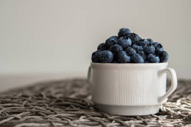 Water drops on ripe blueberries in small white dish on gray background.
