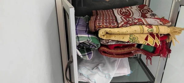 pile of prayer mats, which are arranged in a glass cupboard, which is in the prayer room.