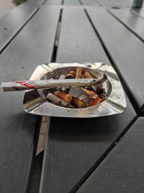 Çöp ve sigara izmaritleriyle dolu alüminyum bir kül tablası ahşap bir masada..