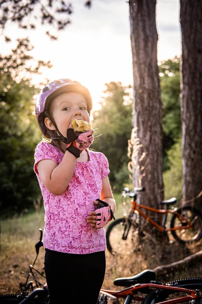 a little girl behind a bicycle eating an apple