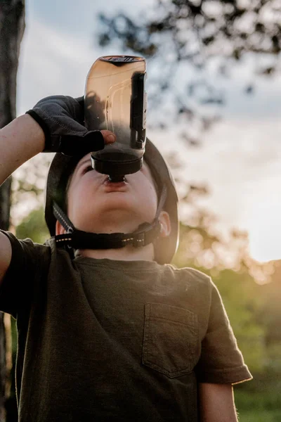 a little boy with a bicycle helmet drinking from a bottle while cycling in the forest