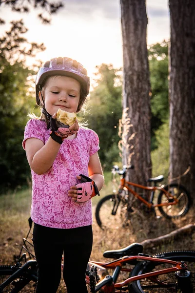 a little girl standing in front of the bicycle eating an apple
