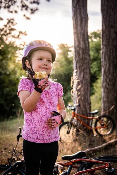 a little girl with a bicycle helmet standing eat an apple