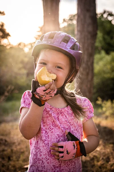a little girl with a bicycle helmet eating an apple