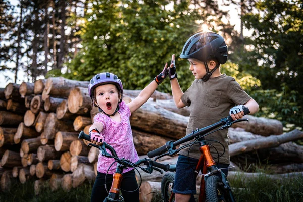 Two funny children with bike helmets give highfive while cycling in the forest