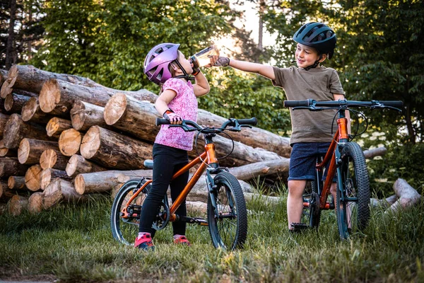 Two children with bike helmets drinking water while cycling in the forest