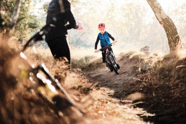 Baba ve oğul sonbaharda ormanda bisiklet sürüyorlar.