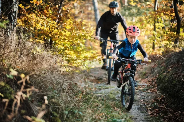 Father and son mountain biking on path in woods autumn