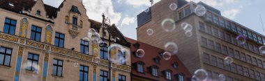 Low angle view of blurred soap bubbles near buildings on urban street in Wroclaw, banner  clipart