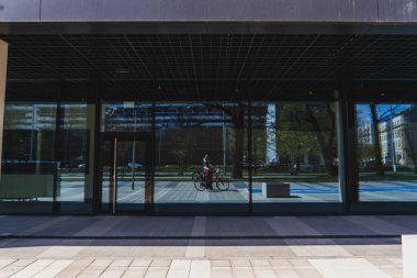 WROCLAW, POLAND - 18 Nisan 2022: Bisikletli kadın şehir caddesindeki binanın ön cephesini yansıtıyor 