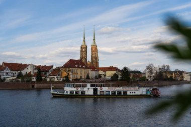 WROCLAW, POLAND - 18 Nisan 2022: Arka planda dolgu iskelesi olan nehir suyu üzerindeki tekne 