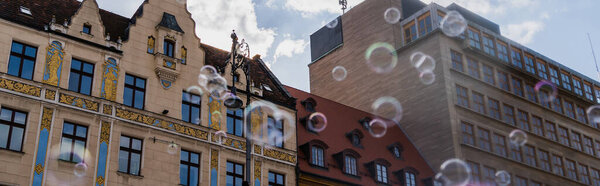 Low angle view of blurred soap bubbles near buildings on urban street in Wroclaw, banner 