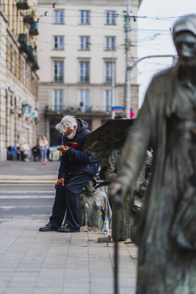 WROCLAW, POLAND - APRIL 18, 2022: Man reading book near Anonymous Pedestrians memorial on urban street 