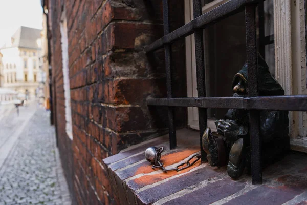 Estatua de gnomo y rejilla cerca de la ventana en la calle urbana en Wroclaw - foto de stock