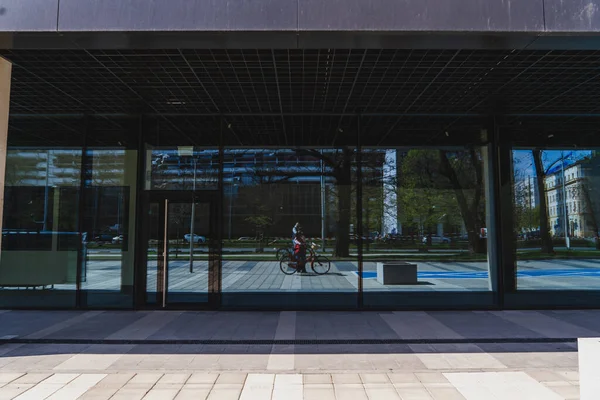 WROCLAW, POLÓNIA - 18 de abril de 2022: Mulher de bicicleta refletindo na fachada da construção na rua urbana — Fotografia de Stock