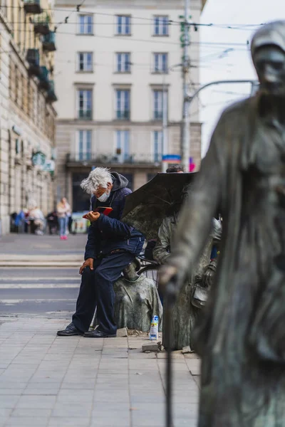 WROCLAW, POLAND - 18 апреля 2022 года: Человек читает книгу возле памятника анонимным пешеходам на городской улице — стоковое фото