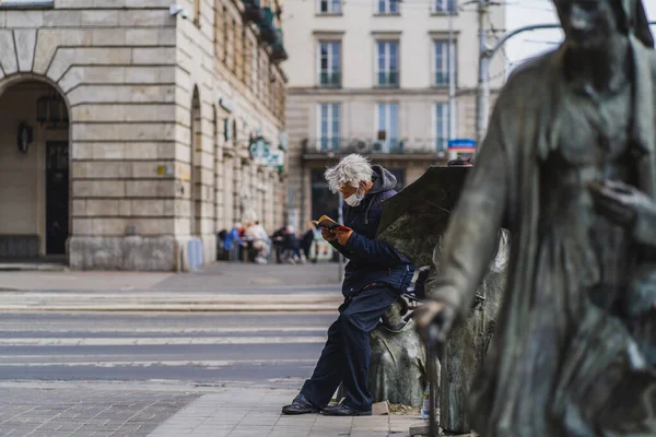 WROCLAW, POLEN - 18. April 2022: Mann mit medizinischer Maske liest Buch in der Nähe des Denkmals der Anonymen Fußgänger auf der städtischen Straße — Stockfoto