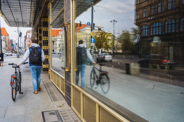 WROCLAW, POLONIA - 18 DE ABRIL DE 2022: Vista trasera del hombre con bicicleta caminando cerca del edificio en la calle urbana - foto de stock