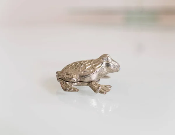 Beyaz yüzeyde izole edilmiş metalden yapılmış küçük bir kurbağaya yakın plan. 