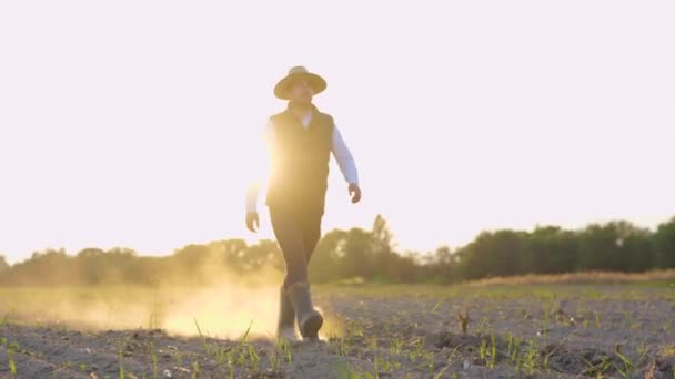 快乐英俊的男性农民穿着橡胶靴在田里穿过绿色的小麦小苗 日落时分 在农场干地上散步的人笑了 农艺学概念 — 图库视频影像