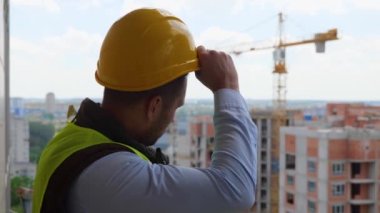 Kafkasyalı profesyonel erkek müteahhit, inşaat alanında dikilip başlığını çıkarırken yüzünü çeviriyor. İnşaat endüstrisi. Şapkalı yakışıklı işçi, iş konsepti.
